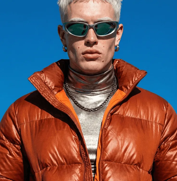 Platinum-haired model in an orange puffer against a cobalt sky